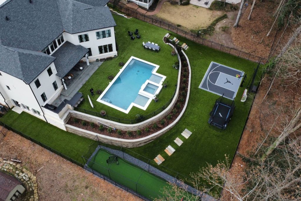 Drone shot of artificial grass backyard with pool and basketball court